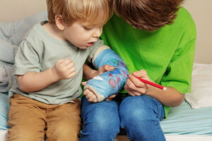 A young boy signs his younger brother's cast