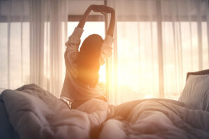 A young woman stretches arms overhead as she greets the sunrise
