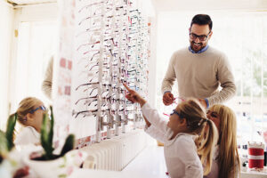 Two young girls try on different glasses at the optomitrist