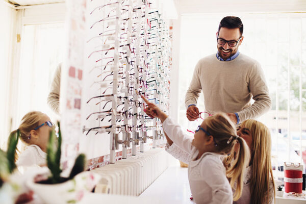 Two young girls try on different glasses at the optomitrist