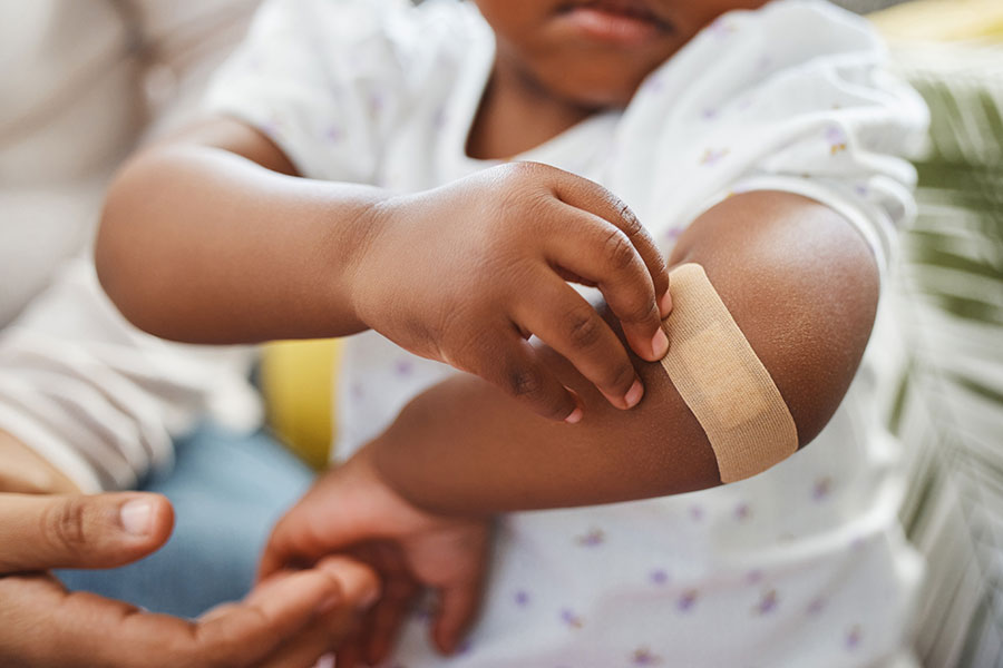 A little girl fusses with a bandage on her elbow.