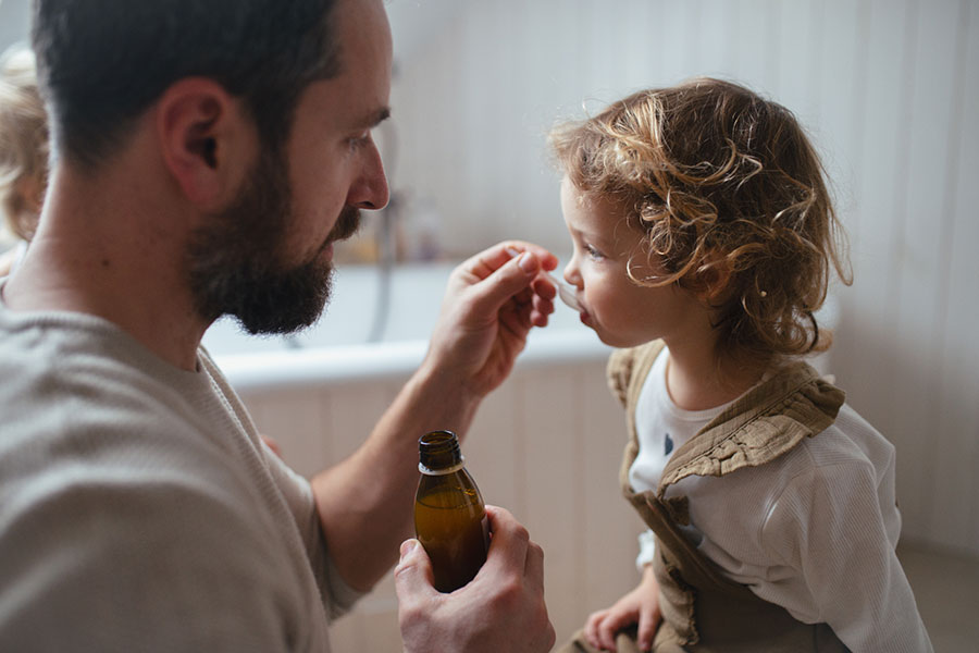 A father gives a spoonful of medicine to his daughter