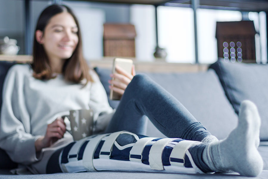 A young woman with her leg in a brace rests on couch